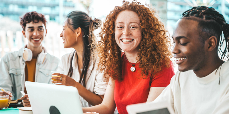 four people smiling sitting around a computer